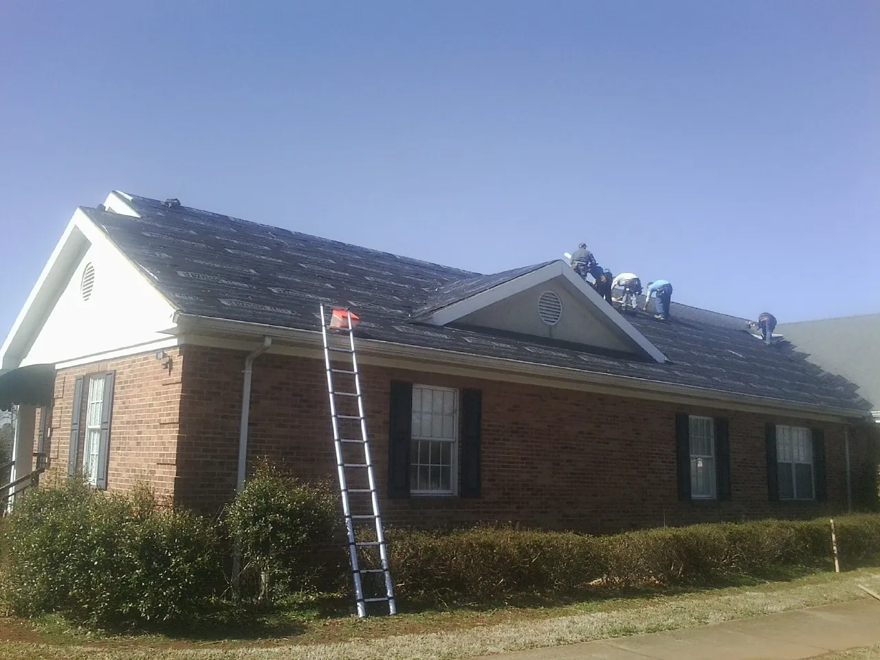 Crew tearing shingles off a brick ranch roof with a ladder set — Metal Roof Repair work by our crew in Cuba