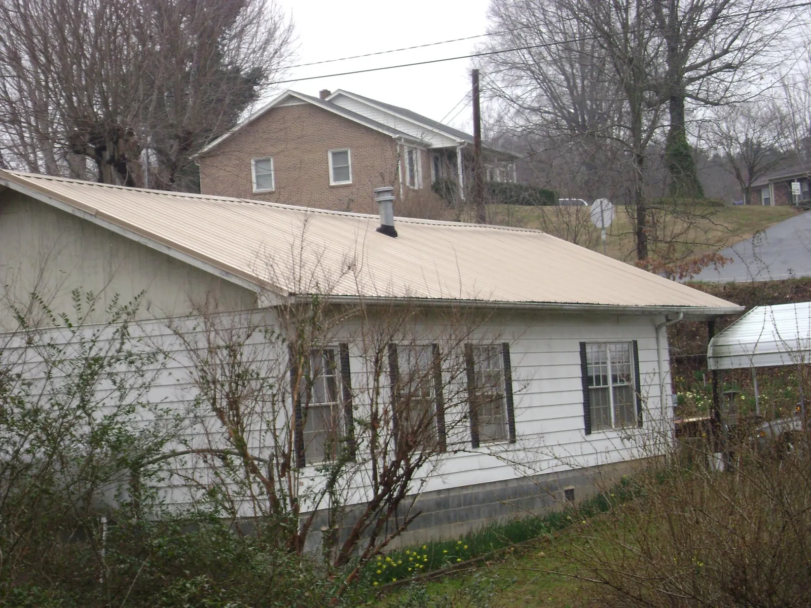 Tan metal roof on a white sided house set into a hillside — Commercial Roofing by Roofing Brothers in Cuba